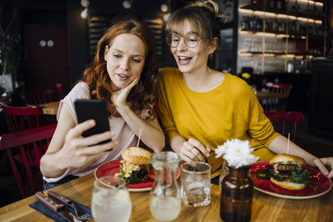 Two female friends with cell phone having burger in a restaurant stock photo