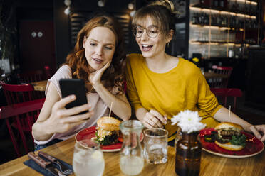 Zwei Freundinnen mit Handy essen einen Burger in einem Restaurant - KNSF06659