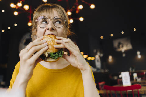 Junge Frau isst Burger in einem Restaurant, lizenzfreies Stockfoto