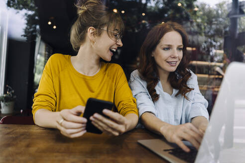 Two female friends with laptop and cell phone in a cafe - KNSF06669