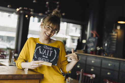 Young woman in a restaurant holding 'wait to be seated' sign - KNSF06670