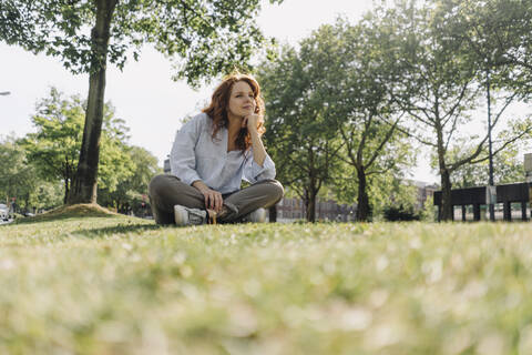 Rothaarige Frau sitzt auf einem Grünstreifen, lizenzfreies Stockfoto
