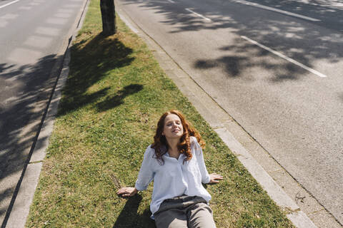 Redheaded woman sitting on grass verge stock photo
