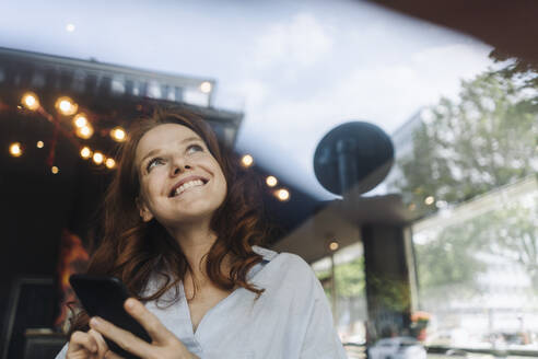 Glückliche rothaarige Frau mit Mobiltelefon in einem Café - KNSF06678