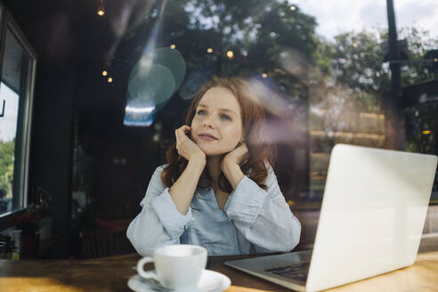 Redheaded woman with laptop in a cafe thinking - KNSF06679