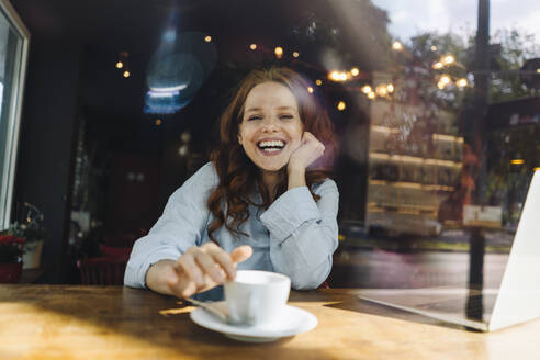 Portrait of happy redheaded woman with laptop in a cafe - KNSF06680