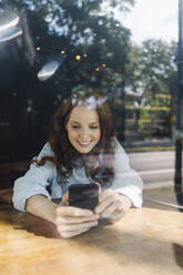 Glückliche rothaarige Frau mit Mobiltelefon in einem Café - KNSF06681