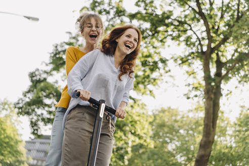 Happy female friends riding e-scooter together - KNSF06683