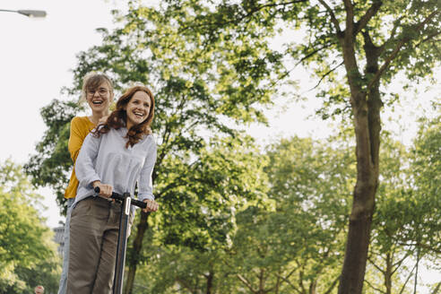 Glückliche Freundinnen fahren gemeinsam E-Scooter - KNSF06684