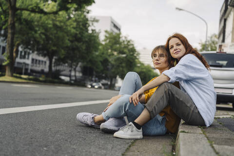 Freundinnen sitzen am Straßenrand in der Stadt, lizenzfreies Stockfoto