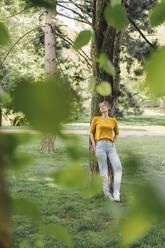 Junge Frau lehnt an einem Baum im Park - KNSF06696