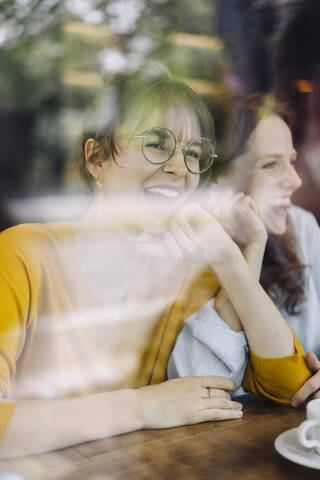 Zwei glückliche Freundinnen hinter der Fensterscheibe eines Cafés, lizenzfreies Stockfoto