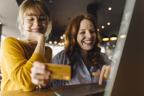 Two happy female friends with laptop and credit card in a cafe - KNSF06709