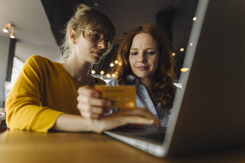 Two female friends with laptop and credit card in a cafe - KNSF06710