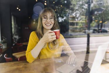 Portrait of smiling woman with laptop and coffee in a cafe - KNSF06714