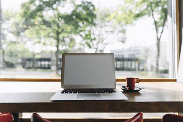 Laptop und Tasse Kaffee auf einem Tisch in einem Café - KNSF06717