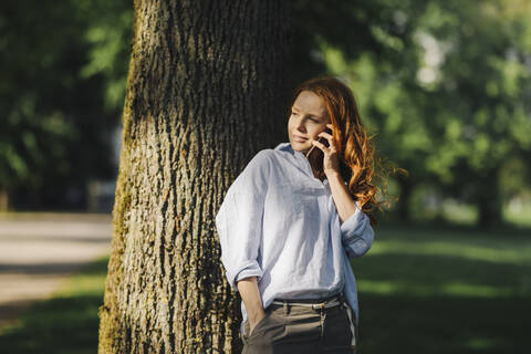 Rothaarige Frau beim Telefonieren im Park, lizenzfreies Stockfoto