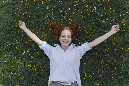Porträt einer glücklichen rothaarigen Frau, die auf einer Blumenwiese liegt - KNSF06729