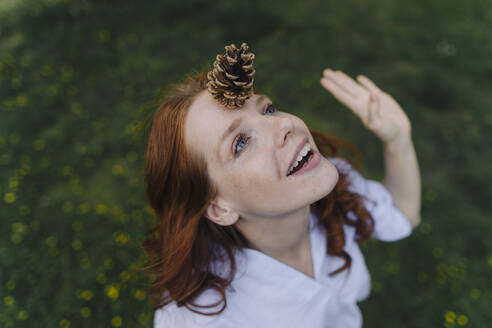 Redheaded woman balancing a pine cone on her forehead - KNSF06730