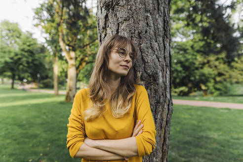 Young woman at a tree in park looking sideways - KNSF06732