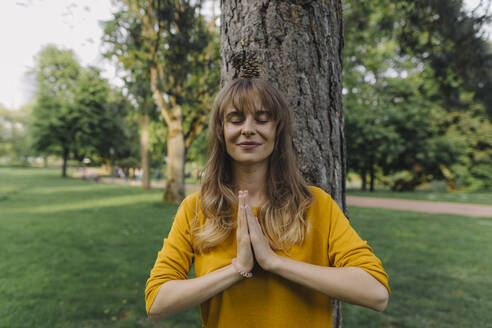 Young woman balancing a pine cone on her head in park - KNSF06733