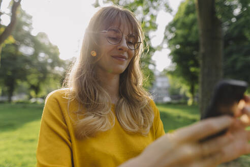 Young woman using cell phone in park - KNSF06734