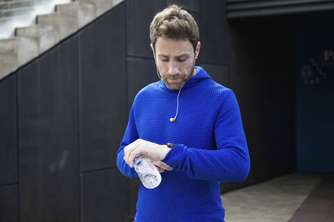 Porträt eines Joggers mit Wasserflasche, der seinen Trainingsfortschritt auf seiner Smartwatch überprüft, lizenzfreies Stockfoto