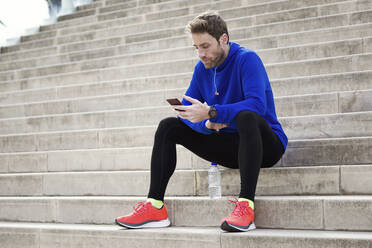 Jogger sitzt auf den Stufen und benutzt sein Smartphone - JSRF00653