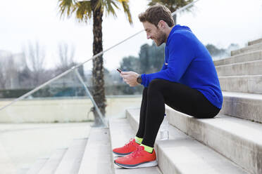 Jogger sitting on steps and using smartphone - JSRF00654