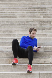 Jogger sitzt auf den Stufen und benutzt sein Smartphone - JSRF00658