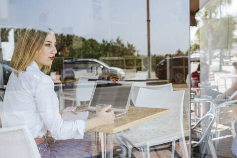 Junge Frau mit Laptop auf einem Tisch in einem Café und Blick aus dem Fenster, lizenzfreies Stockfoto