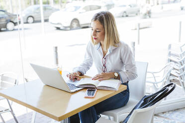 Junge Frau mit Laptop und Notizbuch auf einem Tisch in einem Cafe - LJF01050