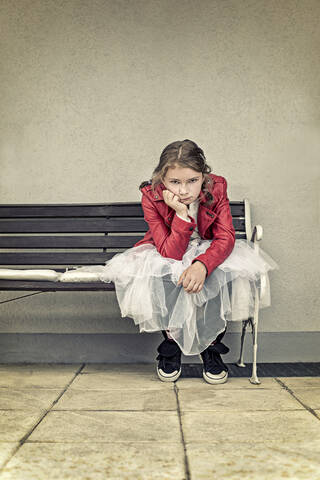 Portrait of unhappy girl wearing red leather jacket and tutu sitting on bench stock photo