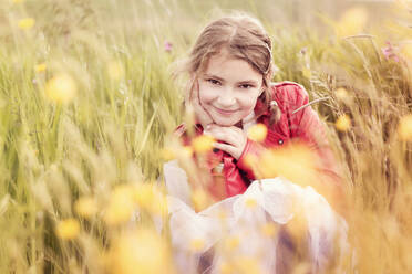 Porträt eines lächelnden Mädchens in roter Lederjacke, das in einer Blumenwiese hockt - STBF00411
