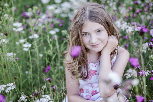 Porträt eines lächelnden Mädchens, das auf einer Blumenwiese sitzt - STBF00421