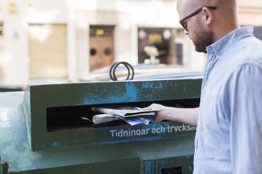 Mann wirft Zeitungen in die Recycling-Tonne - JOHF01353