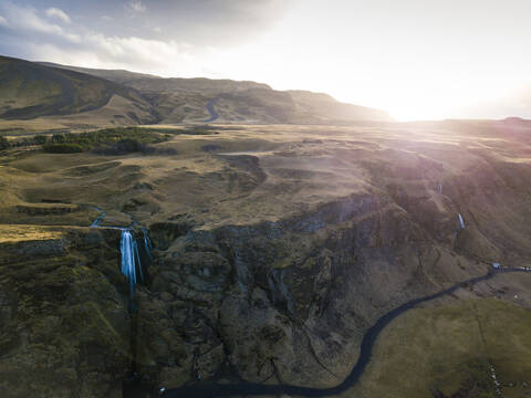 Island, Luftaufnahme eines Wasserfalls, der bei Sonnenuntergang eine hohe Klippe hinabstürzt, lizenzfreies Stockfoto