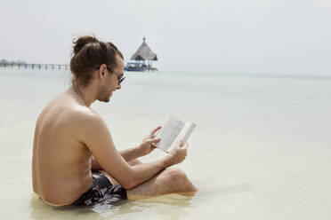 Man on beach reading book - JOHF01690