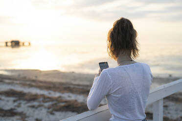 Junge Frau fotografiert Sonnenuntergang am Strand - JOHF01779