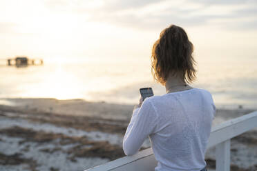 Young woman photographing sunset on beach - JOHF01779