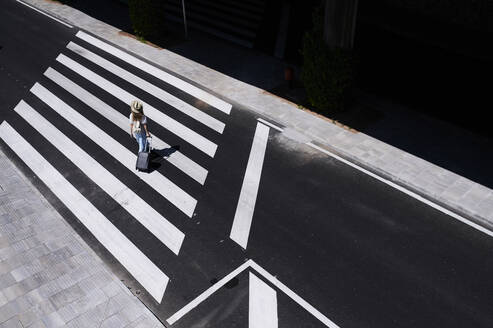 Top view of young woman with baggage crossing a street at the airport - IGGF01341