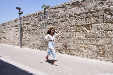 Happy young woman running along a wall - IGGF01351