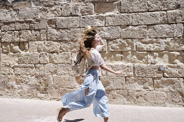 Happy young woman running along a wall - IGGF01352