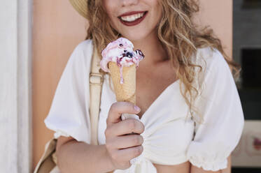 Nahaufnahme einer jungen Frau, die eine schmelzende Eiswaffel im Sommer isst - IGGF01354