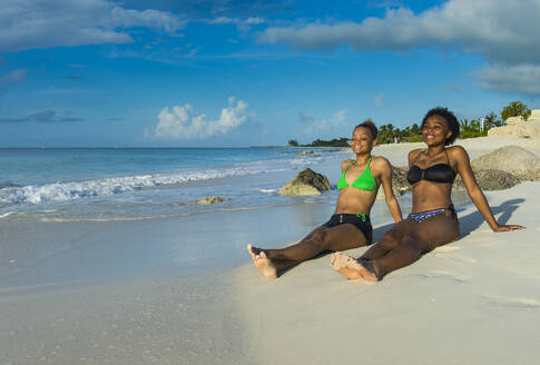 Lächelnde Freundinnen in Bikinis entspannen sich am Strand von Grace Bay bei Sonnenuntergang, Providenciales, Turks- und Caicosinseln - RUNF03345