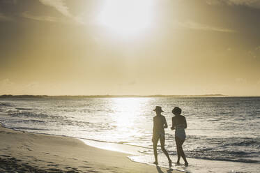 Rückansicht von Freundinnen beim Spaziergang am Strand von Grace Bay bei Sonnenuntergang, Providenciales, Turks- und Caicosinseln - RUNF03347