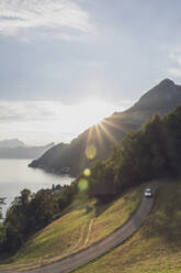 Schweiz, Gersau, Schwyz, Autofahrt auf kurvenreicher Straße bei Sonnenuntergang mit Vierwaldstättersee im Hintergrund - MMAF01126