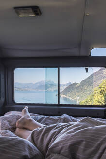 Schweiz, Gersau, Schwyz, Nackte Füße einer schlafenden Person im Wohnmobil mit Vierwaldstättersee durch das Fenster gesehen - MMAF01132