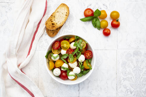 Serviette, Brotscheiben und Schüssel mit frischem Salat liegen auf dem gekachelten Tisch - LVF08290