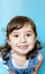 Portrait of cute little girl smiling very expressive on blue background - GEMF03179